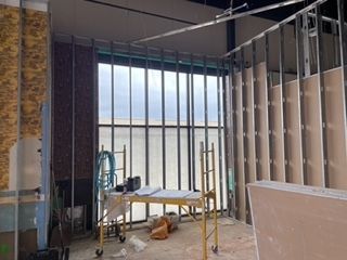 Interior of a building under construction, showing metal studs, windows, and drywall.