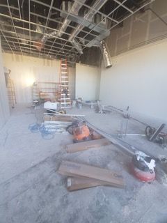 Construction in progress; unfinished ceiling with metal framework; tools and materials scattered on concrete floor.