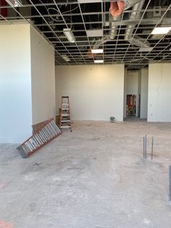 An unfinished interior construction site with a ladder, white walls, and exposed ceiling grid.