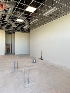 Interior of a room under construction with white walls, exposed ceiling, and concrete floor.