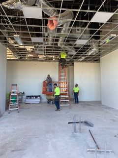 Construction workers in a room with exposed ceiling grid, installing ceiling tiles.