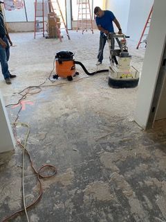 Man using floor grinder; vacuum and debris on a concrete floor during construction.