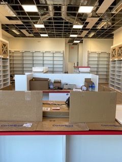Empty retail space with white shelving, open ceiling, and cardboard boxes on a red counter.