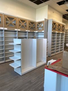 Empty retail shelving; white and tan cabinets with open shelves and decorative wood panels.