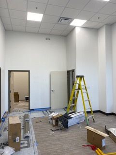 Interior view of an unfinished office space with white walls, doors, and a yellow ladder.