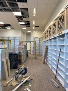 Empty store interior under construction with shelving, tools, and exposed ceiling panels.