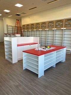 Empty retail store interior with red-topped display tables, shelving, and a ladder.