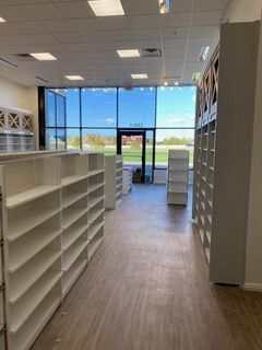 Empty retail space with white shelves and large windows overlooking outdoors.