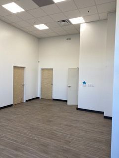 Empty room with light-colored walls, wooden floor, and three doors. Ceiling has recessed lighting.