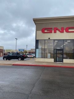 Exterior view of a GNC store on a cloudy day, with a black truck parked outside.