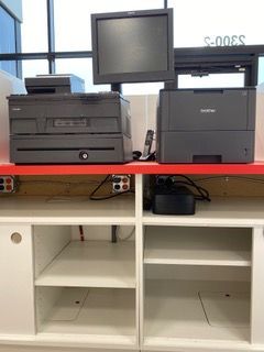 Cash register setup: monitor, printer, cash drawer on red counter above white cabinet.
