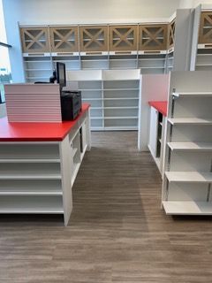 Empty pharmacy interior with red-topped counters, white shelves, and wood-look flooring.