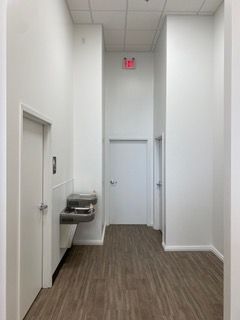 Hallway with white walls, wood-look flooring, doors, and a water fountain.