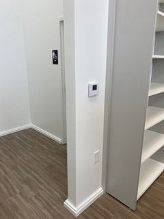 Interior room corner with white walls, wood-look floor, thermostat, and shelving.