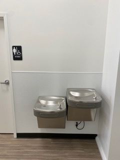 Two stainless steel water fountains on a white wall. Next to a women's restroom sign.