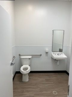 ADA-compliant restroom with white walls, a toilet, sink, mirror, and grab bars.