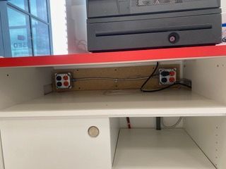 White cabinet interior with electrical outlets, power cables, and a cash register above.