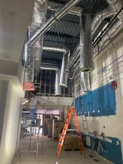 Interior construction scene: ductwork, ladder, boxes, open ceiling, and blue container.