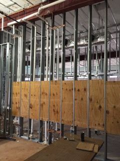 Interior construction site with metal studs, plywood, and plumbing visible.