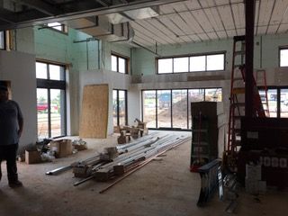 Interior of a building under construction, with windows, materials, and a person standing near the entrance.