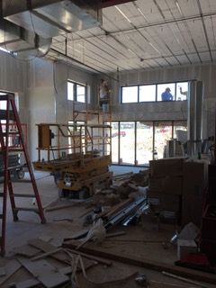 Interior of a building under construction, with workers on a lift, windows, and materials scattered around.