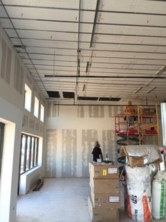 Interior of a building under construction. Drywall installed on walls and ceiling framework. Boxes and tools are present.
