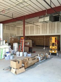 Construction site interior with exposed beams, drywall, and scattered building materials. A small yellow lift sits at the back.