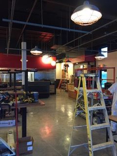 Interior of a restaurant under construction with exposed ceiling, hanging lights, and a ladder.