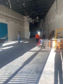 Construction site: Workers in a long, open room with unfinished walls, concrete floor, and equipment.