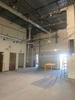 Interior of a building under construction, showing unfinished walls, exposed ceiling infrastructure, doors, and construction equipment.