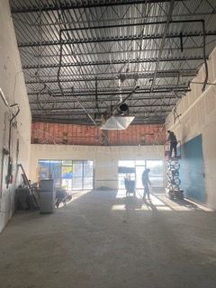 Interior of a building under construction. Workers are present, large windows, exposed ceiling beams and wiring.