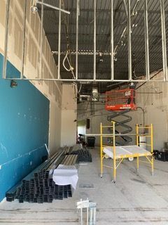 Construction site with metal framing, lift, and scaffolding; blue wall on left.