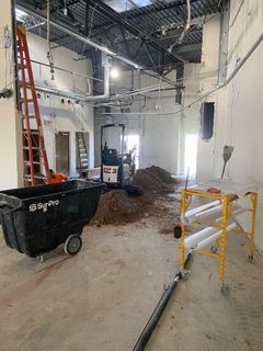 Construction site interior with wheelbarrow, ladder, and small excavator. Dirt pile in the middle.
