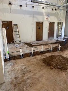 Construction site with plumbing rough-in. Exposed pipes, three brown doors, ladder, and dirt.
