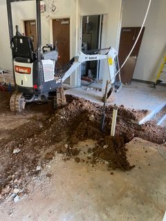 Bobcat excavator digging inside a building, creating a dirt trench.