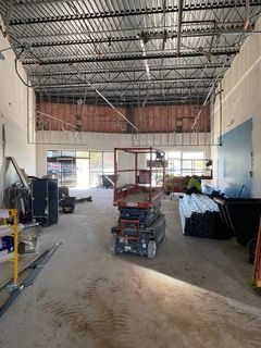 Construction site with exposed ceiling beams, lift, unfinished walls, and a person working.