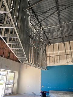 Interior view of construction site with metal framing, partially finished walls, and drywall.