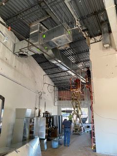 Construction site with HVAC ductwork installed overhead. Workers on a lift. Interior view.