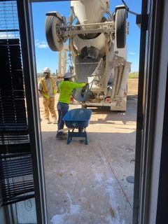 Workers using a cement truck to fill a wheelbarrow on a construction site. Bright sunny day.