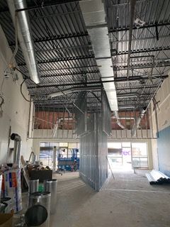 Interior of a commercial building under construction. Metal framework, ducts, and unfinished walls are visible.