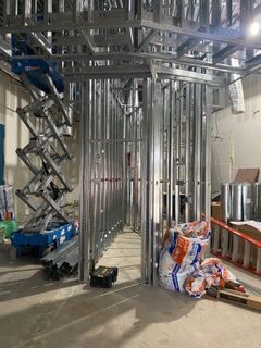 Metal stud framing for walls and ceiling, construction site. Scissor lift and material bags present.