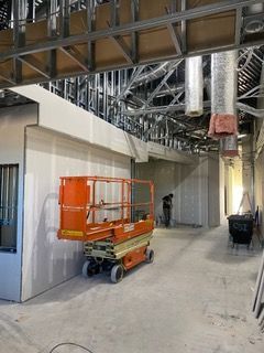Construction site with an orange lift. Drywall is installed on walls and ceiling.