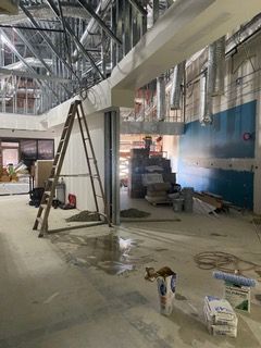 Construction site interior; ladder leans against unfinished wall; exposed metal framework overhead; concrete floor.