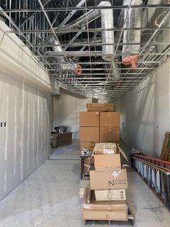 Construction site hallway with drywall walls, exposed metal ceiling framing, and boxes stacked on a pallet.