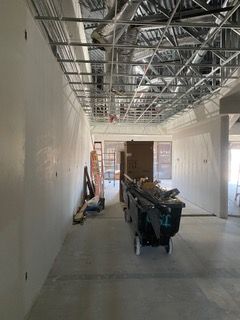 Interior view of a building under construction, showing unfinished walls, ceiling framework, and a rolling cart.
