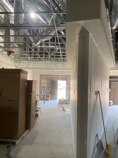Interior view of a construction site with exposed ceiling, drywall, cardboard boxes, and open doorway.
