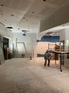 Interior construction site with a worker standing. White walls, exposed ceiling, and tools visible.