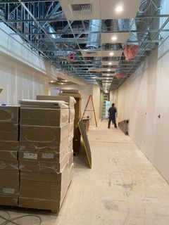 Construction site: corridor with stacked boxes, exposed ceiling framing, and a worker in the distance.