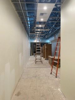 Hallway under construction with ladders, unfinished ceiling, and drywall.
