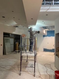 Construction worker sanding ceiling on scaffolding in an unfinished interior space.